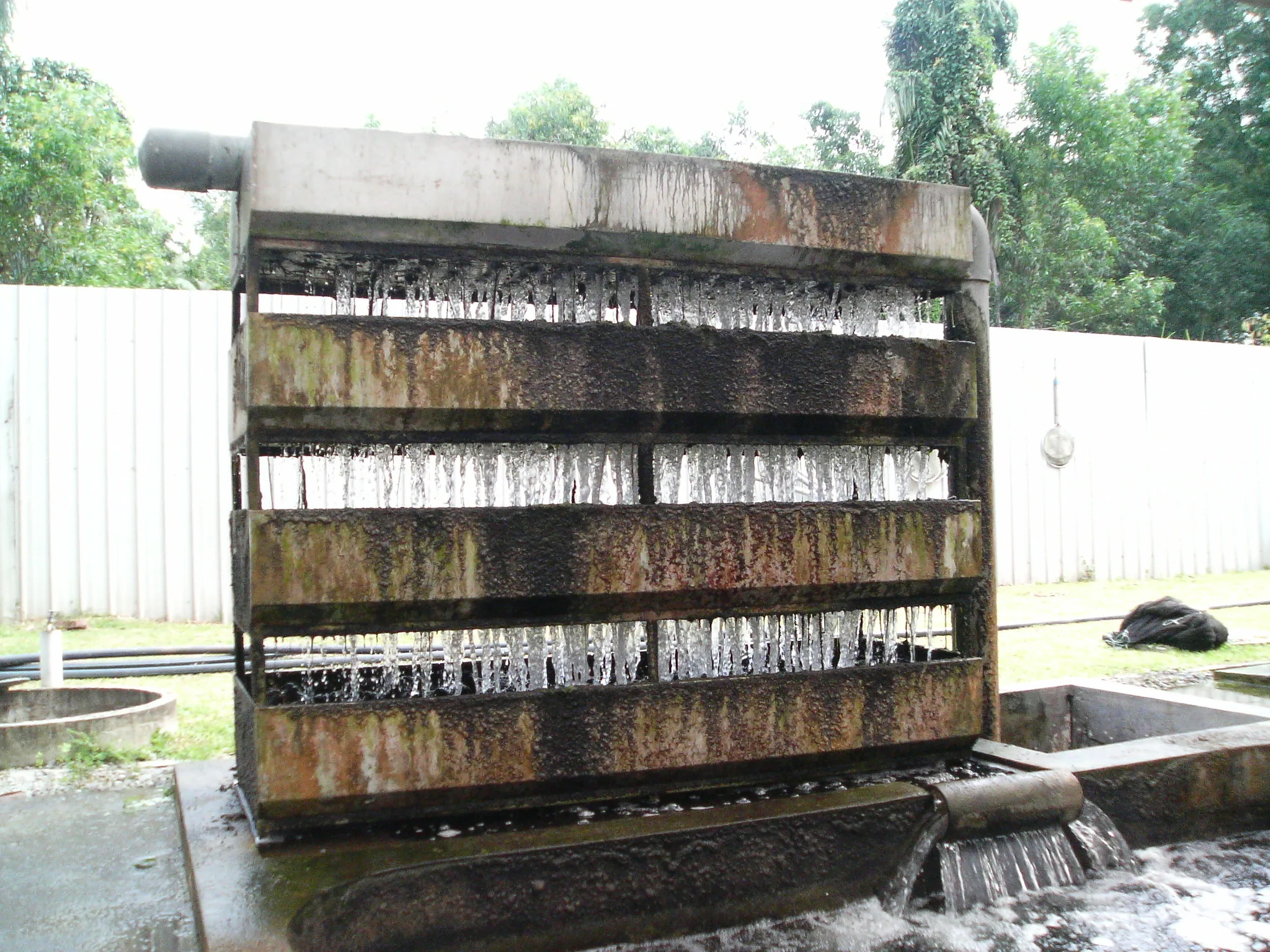 Outdoor koi pond trickle filter with water flowing through several open media trays.